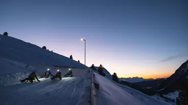 Eine Familie ist bei Sonnenuntergang am Rodeln mit Stirnlampen 