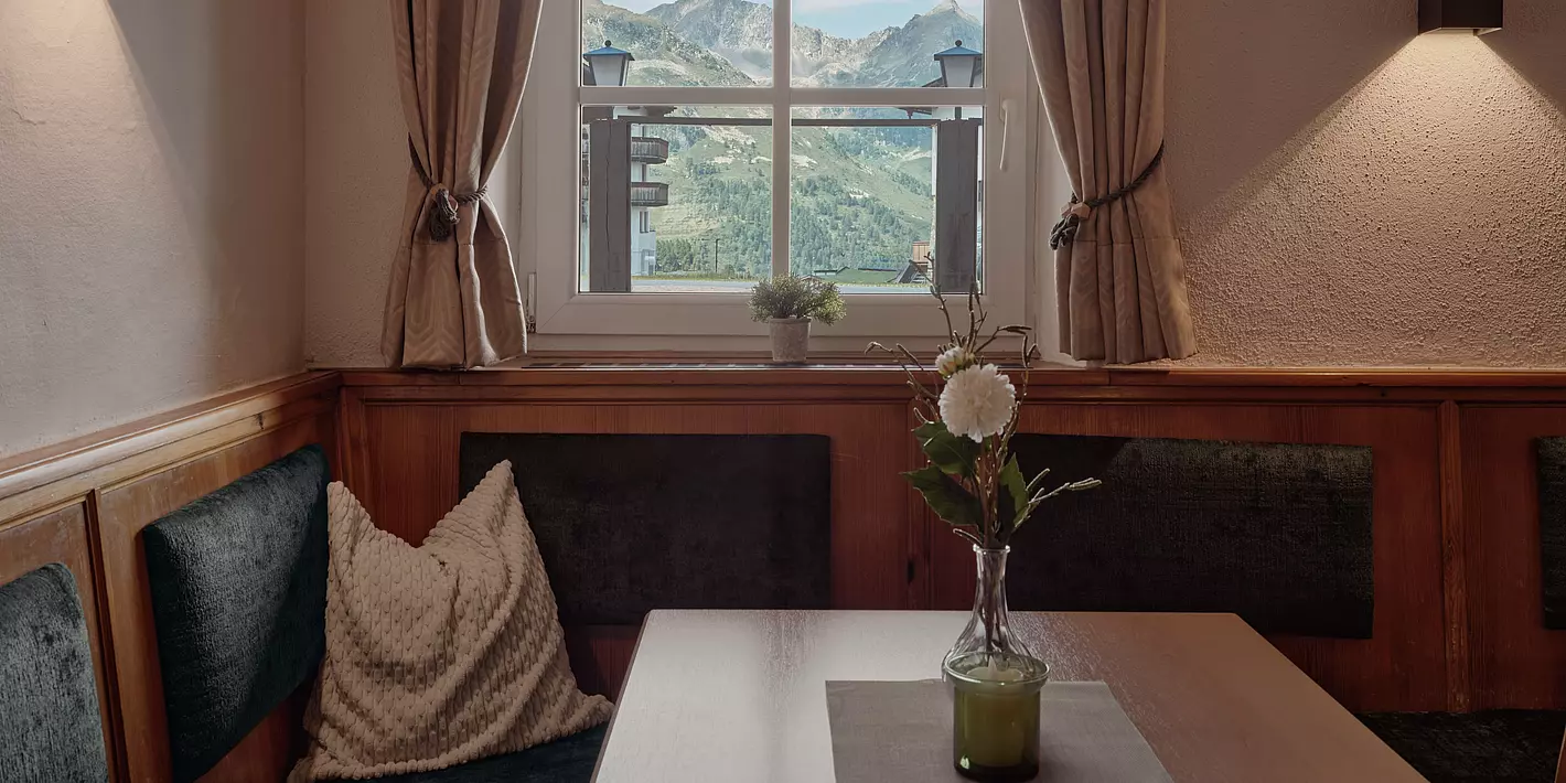 Eckbank mit kleinem Holztisch vor einem Fenster mit Ausblick auf das Bergpanorama