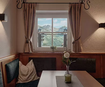 Eckbank mit kleinem Holztisch vor einem Fenster mit Ausblick auf das Bergpanorama