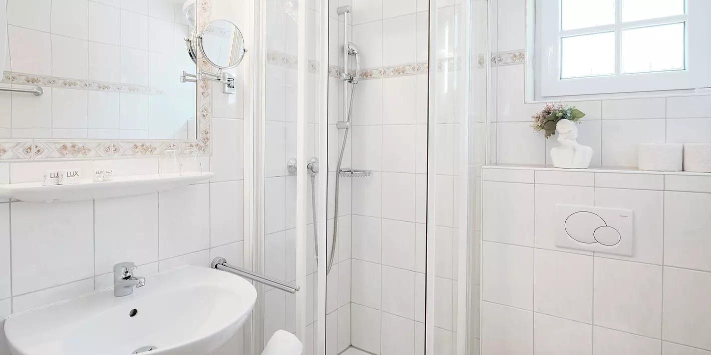 Badezimmer mit Waschbecken, Dusche, Toilette, Spiegel und kleinem Fenster alles in der Farbe weiß