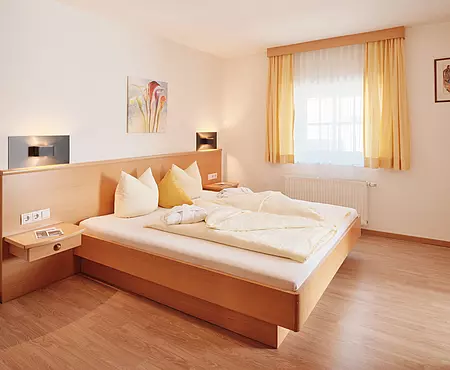 Zimmer mit Doppelbett aus Holzrahmen mit kleinem Fenster und Holzboden