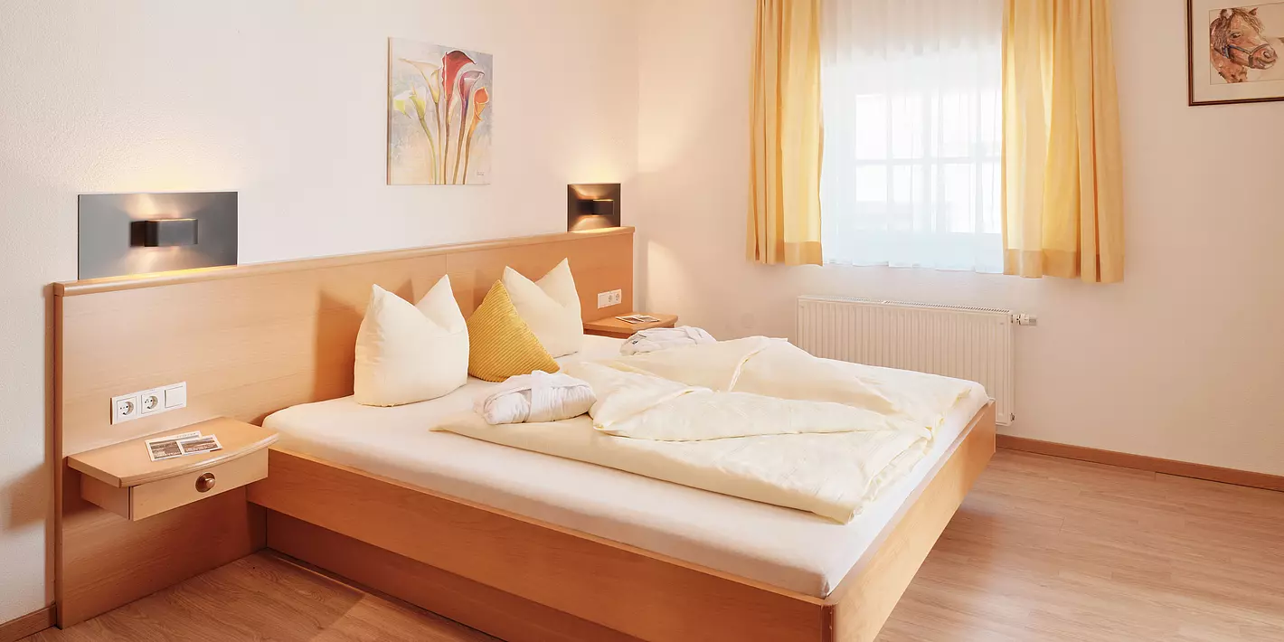 Zimmer mit Doppelbett aus Holzrahmen mit kleinem Fenster und Holzboden